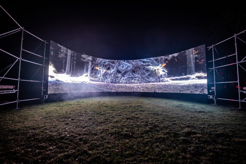 Groot gebogen scherm op een grasveld met een projectie van witte lijnen, Schemerlicht Festival 2024